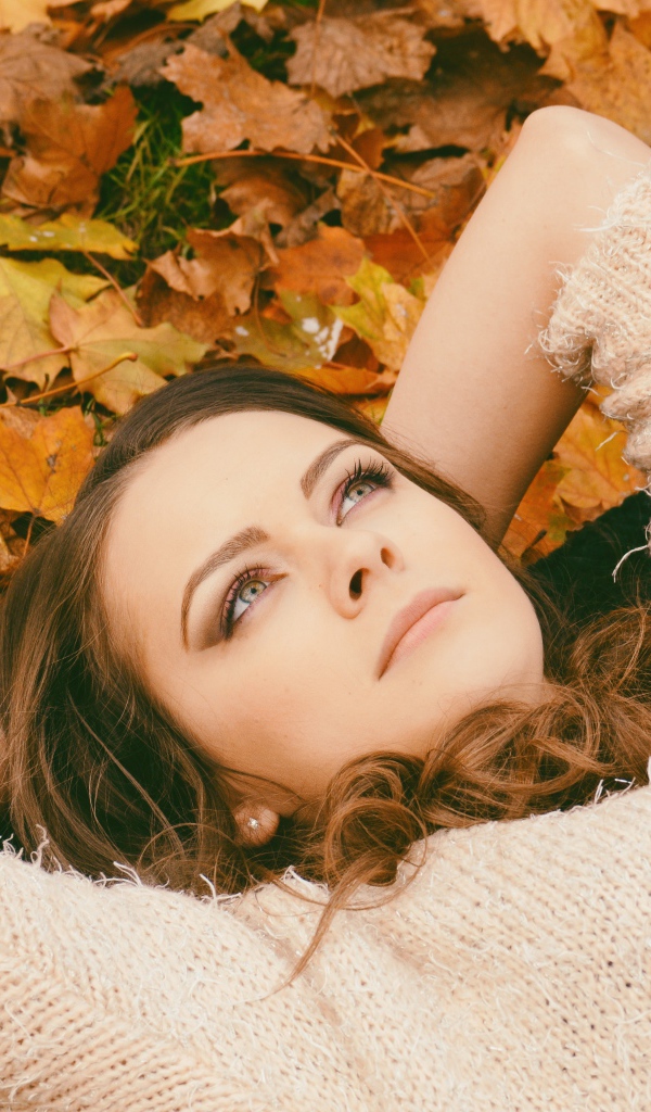 Мечтательная девушка в свитере лежит на земле