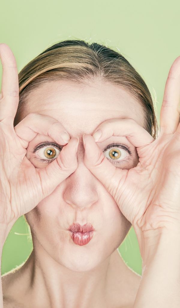 Смешная девушка делает руками очки на лице