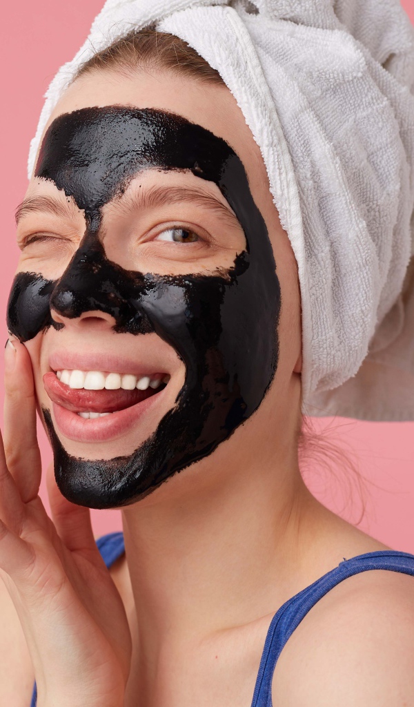 Смешная молодая девушка с черной косметической маской на лице 