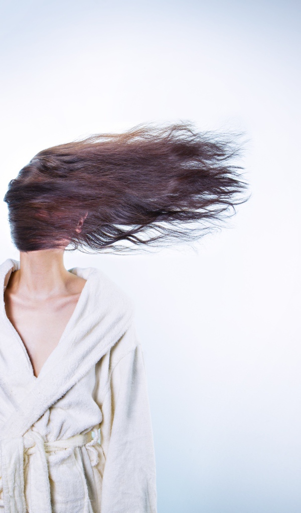 Девушка сушит волосы феном на сером фоне