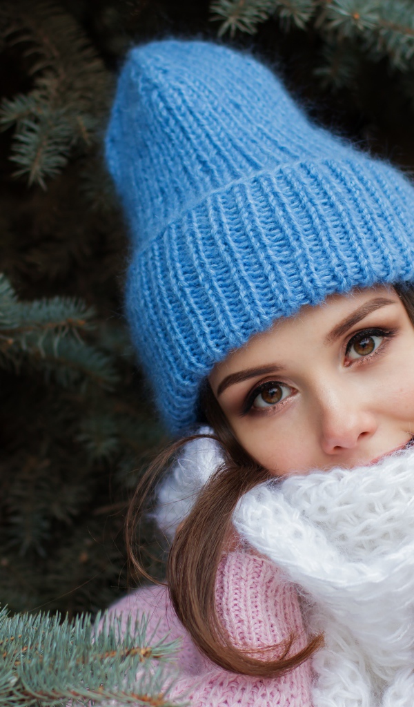 Девушка в голубой вязаной шапке у ели