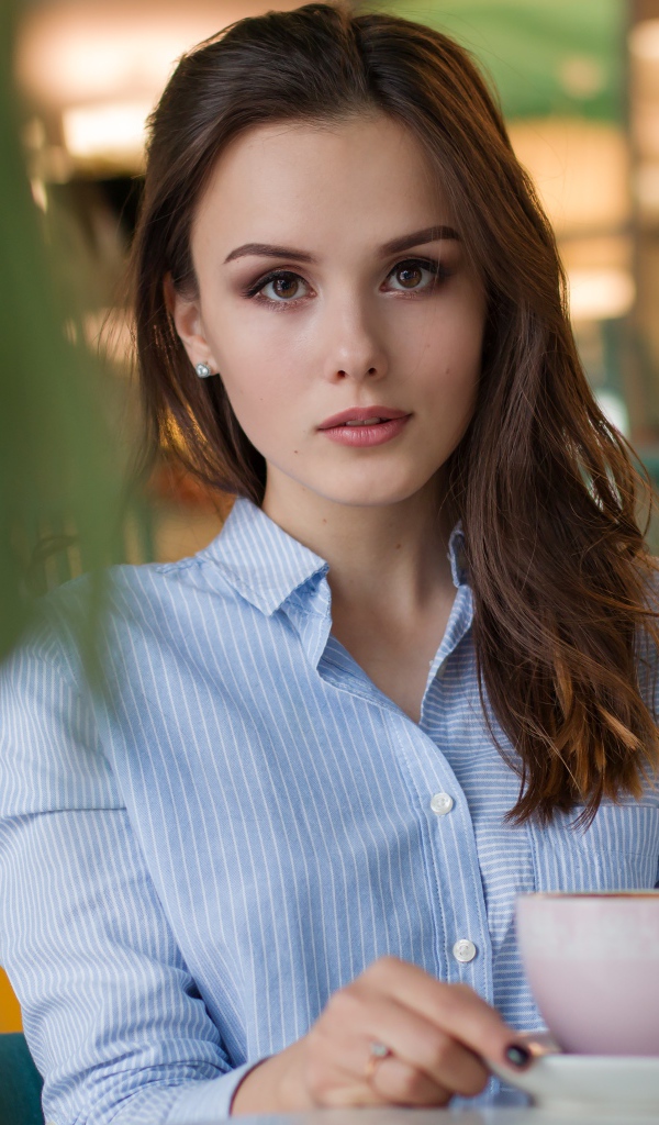 Девушка в голубой рубашке с чашкой кофе на столе в кафе