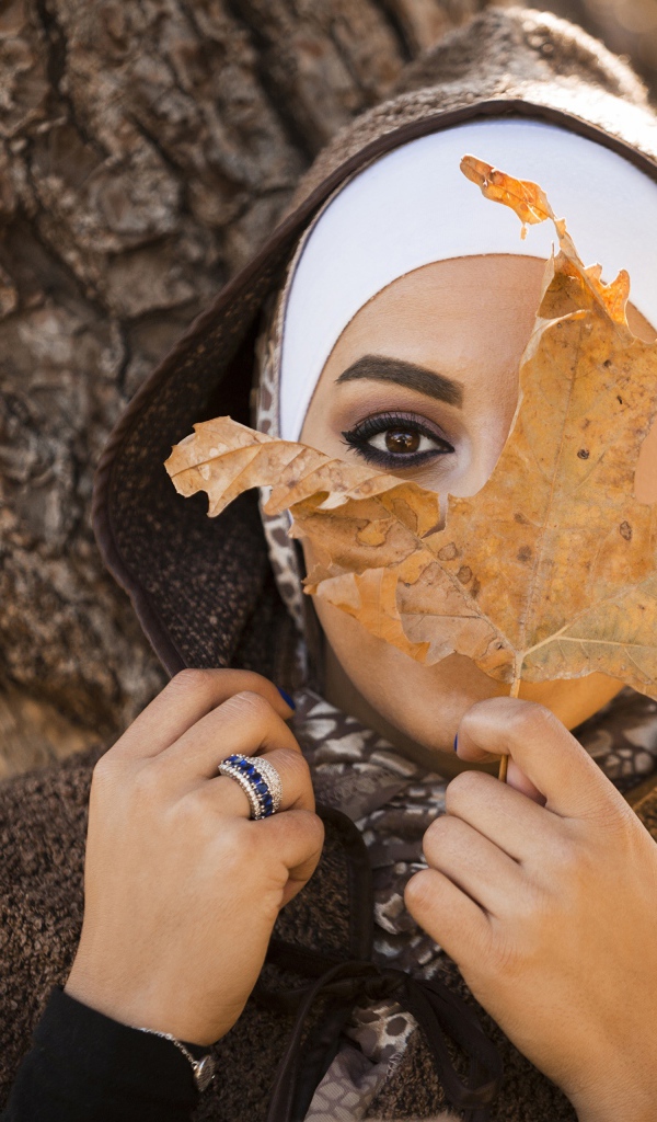 Девушка в пальто с закрывает лицо листом