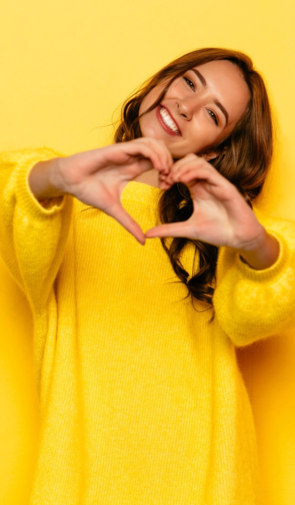Девушка в желтом свитере показывает сердце руками