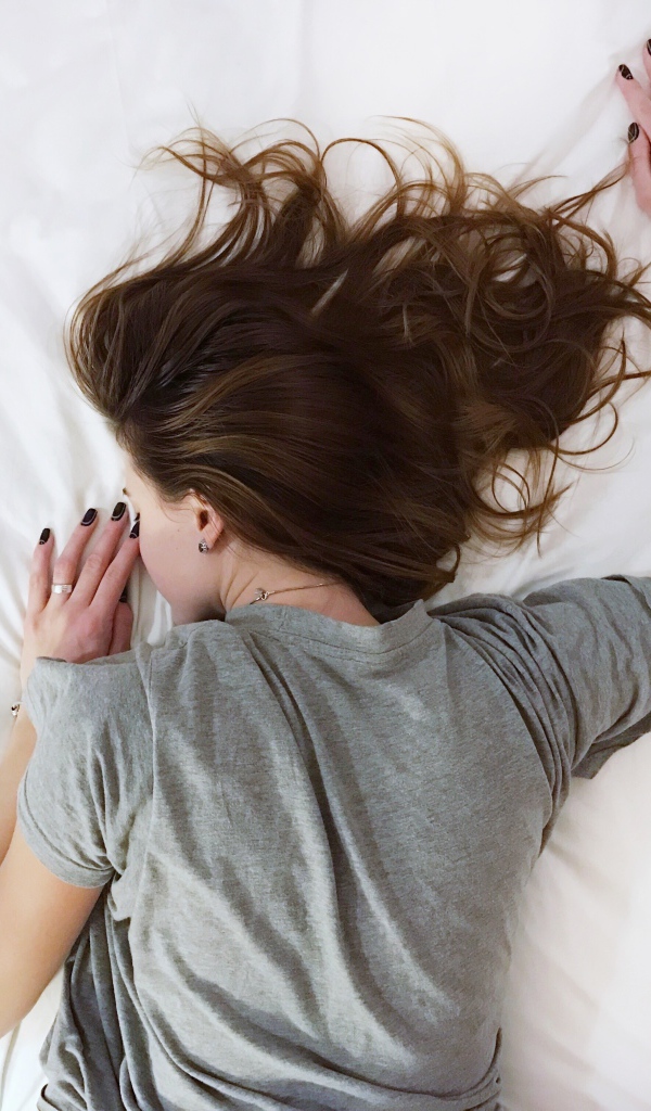 Девушка в серой пижаме спит на кровати 