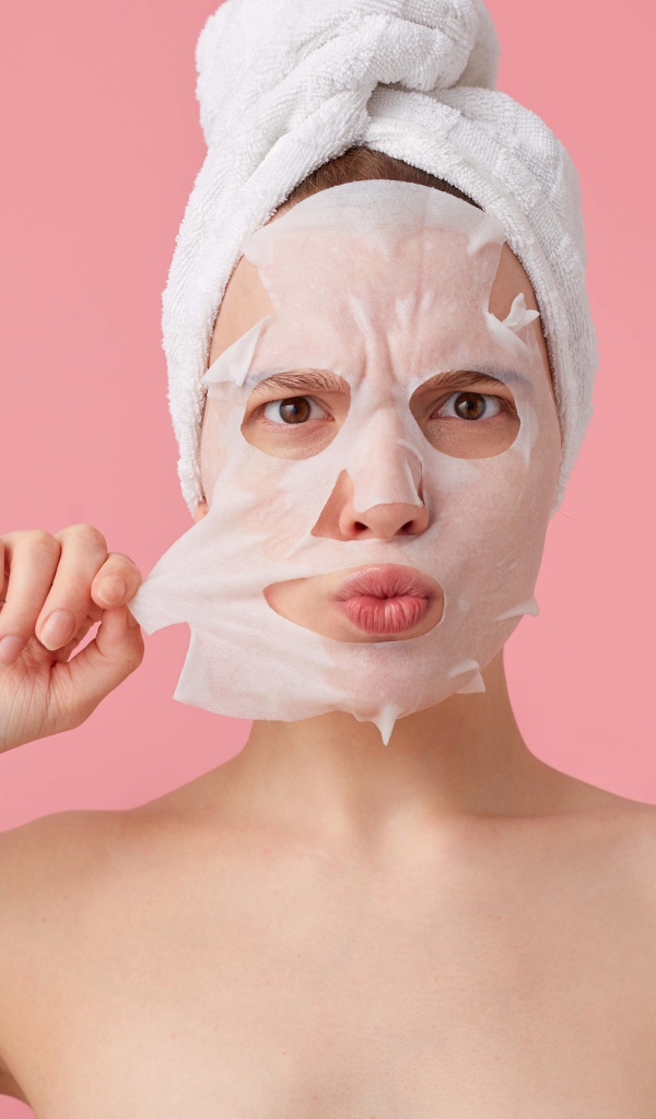 Девушка снимает косметическую маску с лица на розовом фоне 