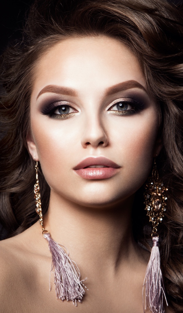 Девушка с прической с красивыми сережками на сером фоне 