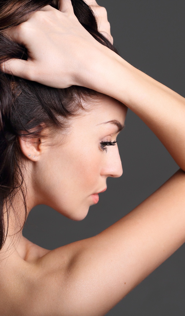 Девушка с руками в волосах на сером фоне