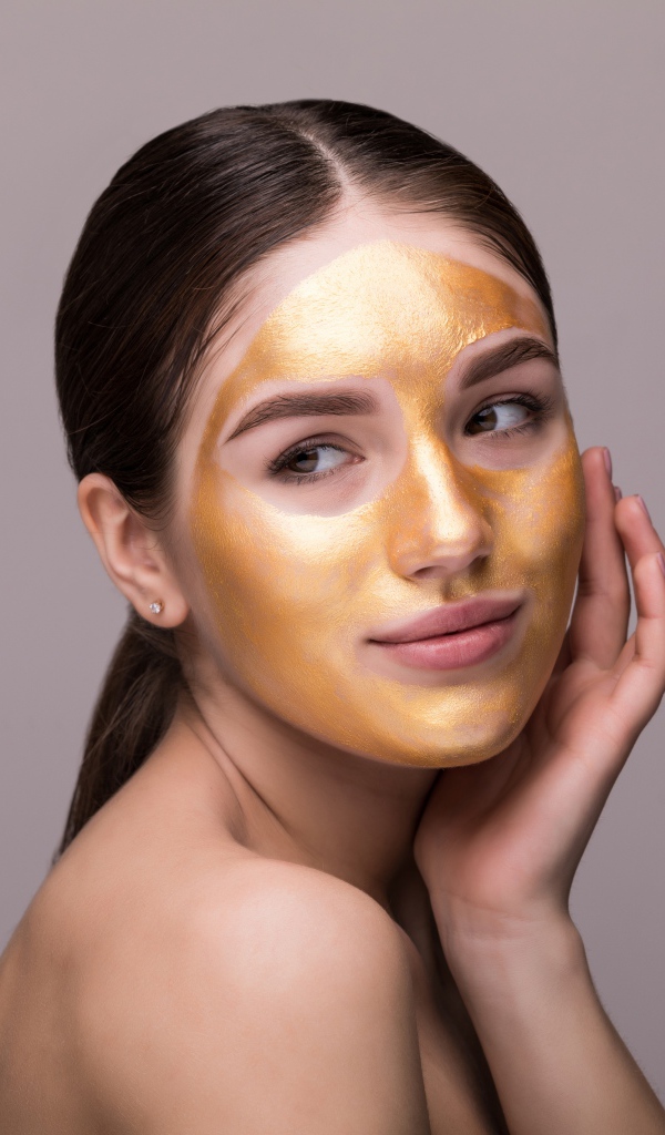 Золотая маска на лице у молодой девушки 