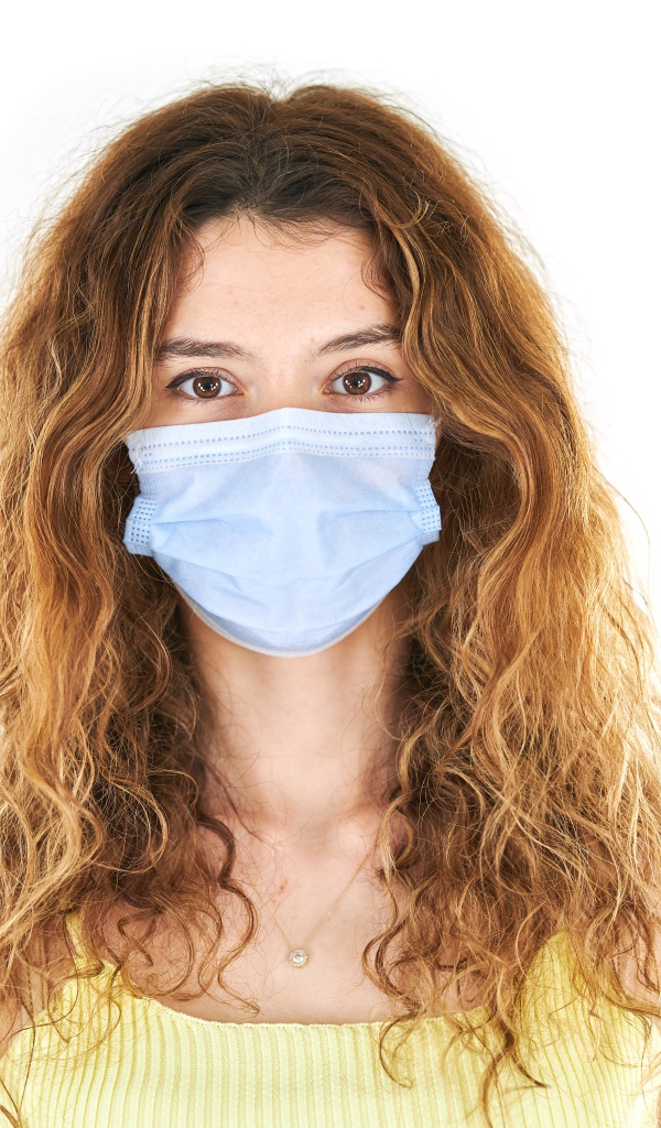 Длинноволосая девушка в маске от коронавируса на белом фоне