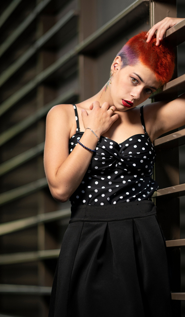 Эпатажная девушка с короткой стрижкой стоит у забора 