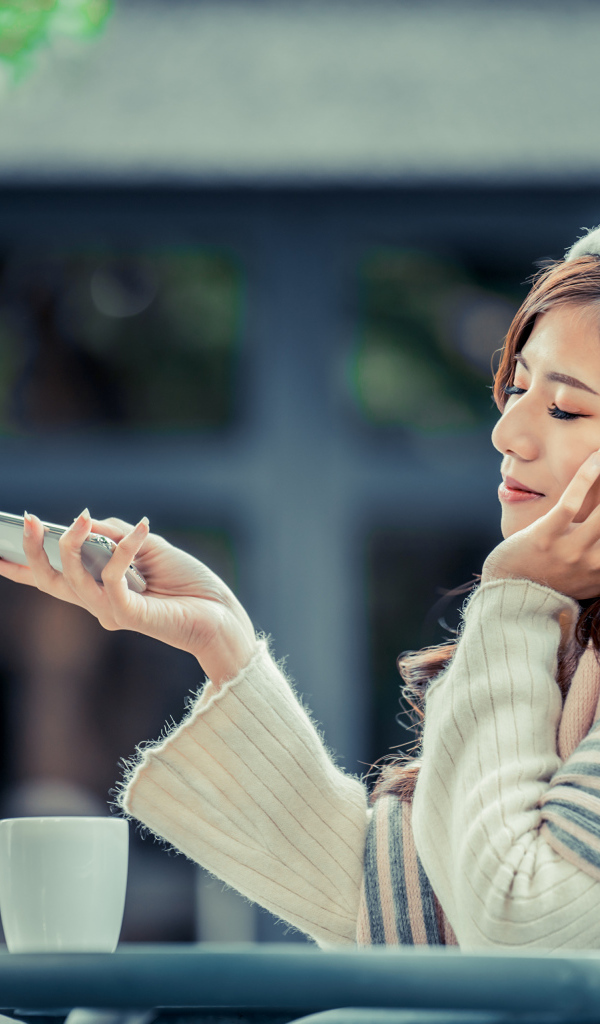 Мечтательная девушка с телефоном сидит в кафе 