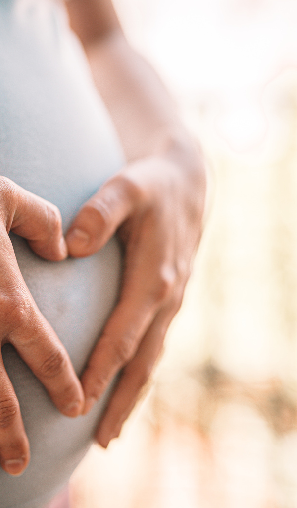 Беременная женщина держит руки на животе 