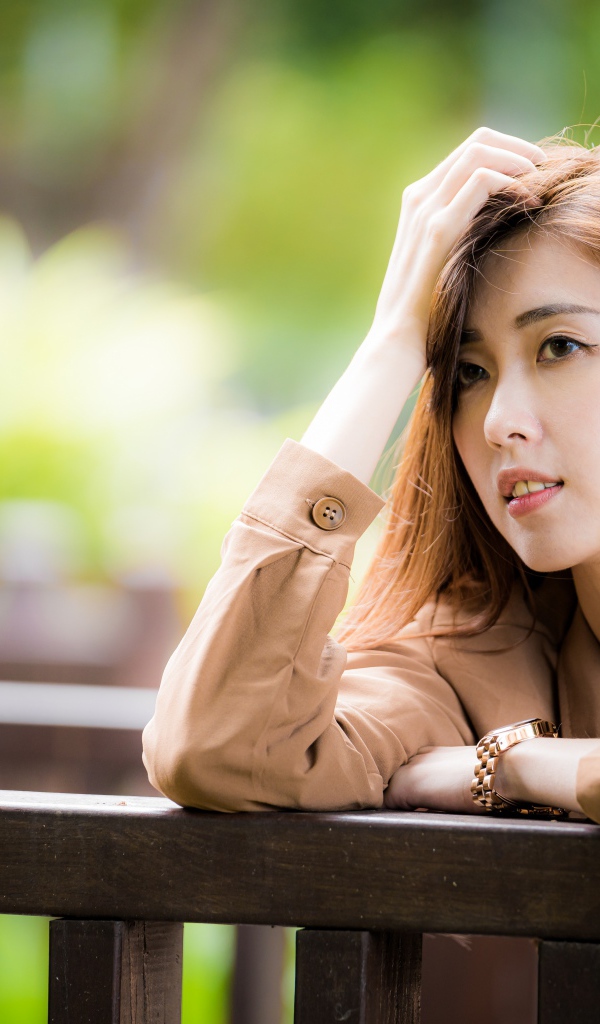 Грустная девушка азиатка стоит у деревянных перил 