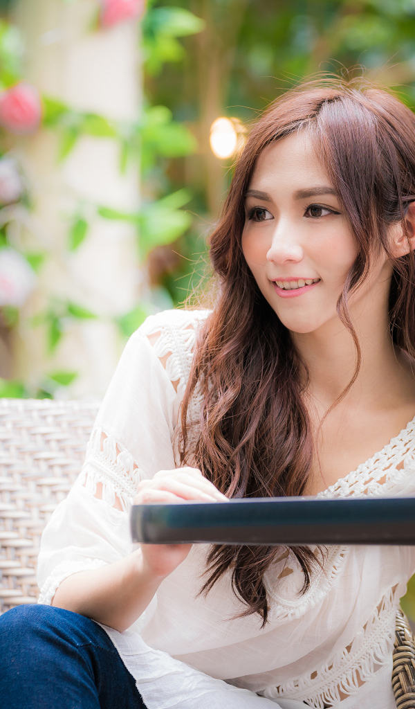 Улыбающаяся девушка азиатка сидит за столом в кафе