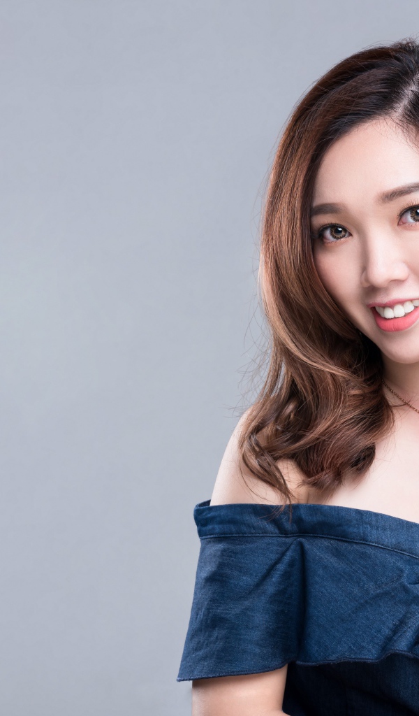 Улыбающаяся девушка азиатка с часами на руке на сером фоне