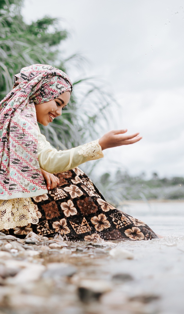 Улыбающаяся девушка азиатка сидит у воды