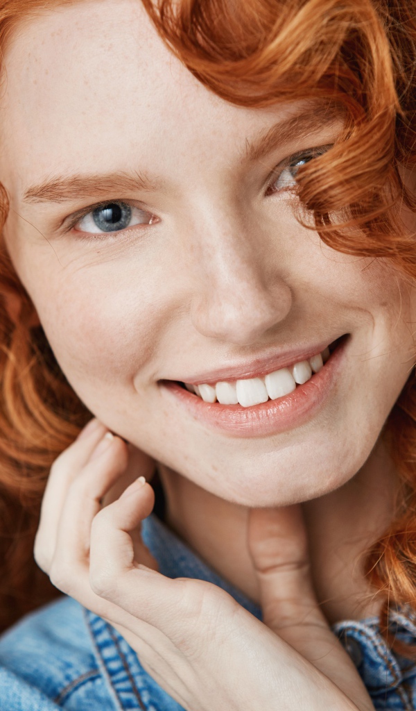 Улыбающаяся голубоглазая рыжеволосая девушка в джинсовой куртке 