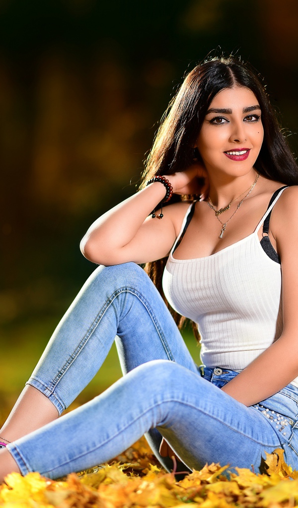 Улыбающаяся брюнетка сидит на опавшей листве