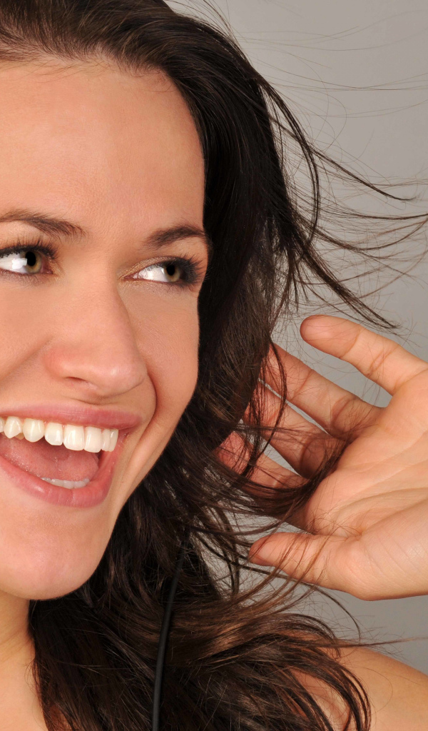 Улыбающаяся девушка в наушниках на сером фоне 