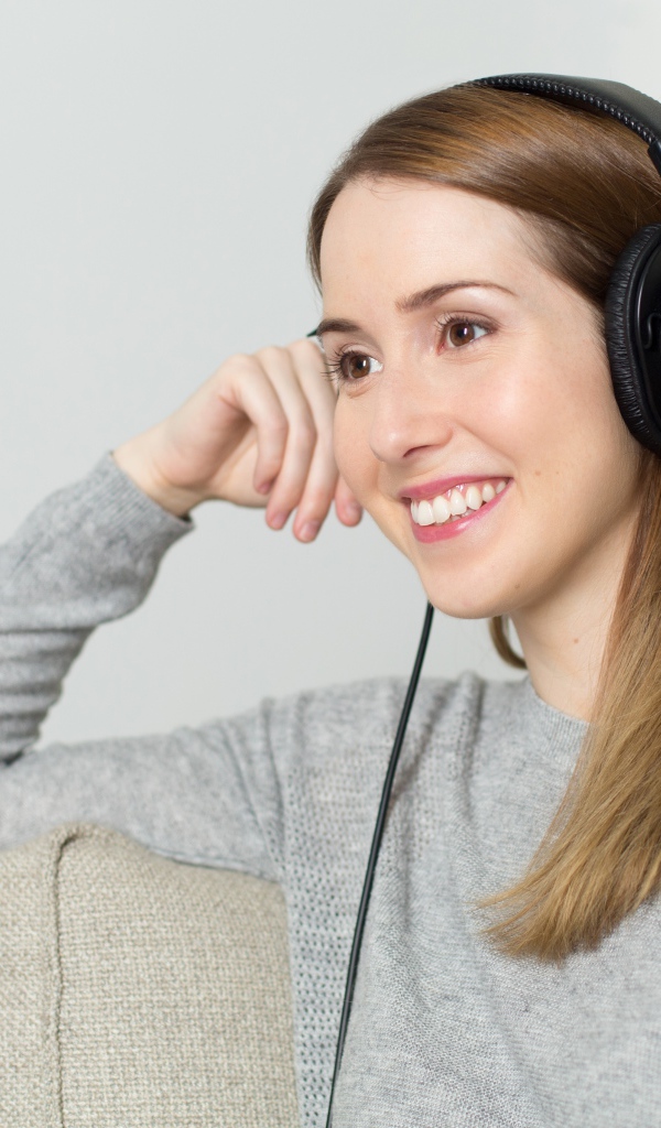 Улыбающаяся девушка в наушниках на диване