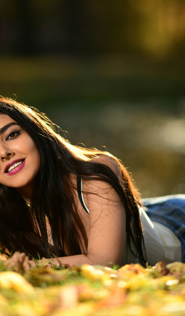 Улыбающаяся девушка модель лежит на земле с опавшими листьями