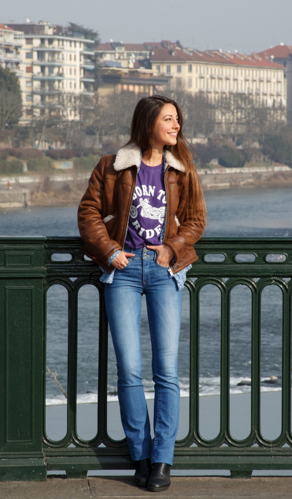 Улыбающаяся девушка стоит на мосту у реки