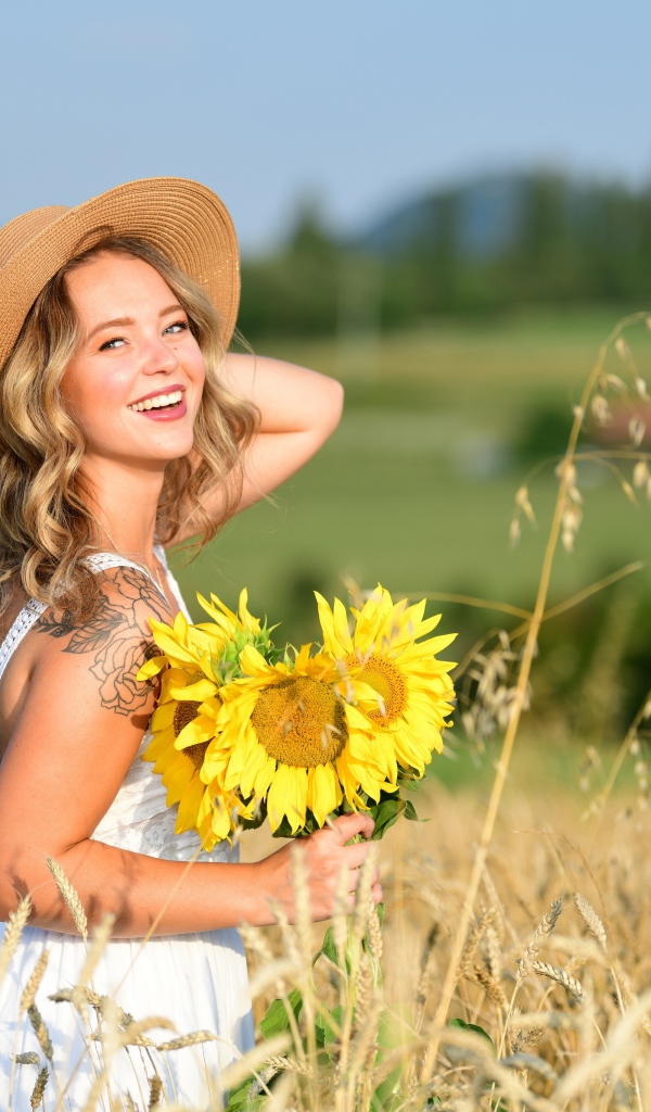 Улыбающаяся девушка с букетом подсолнухов на поле пшеницы