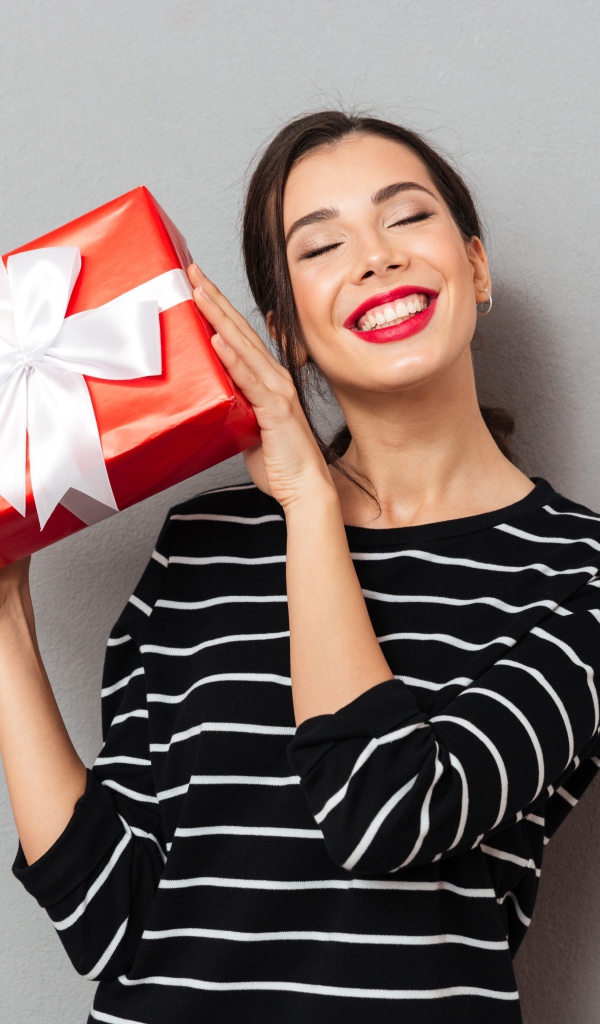 Улыбающаяся девушка с подарком в руках на сером фоне 