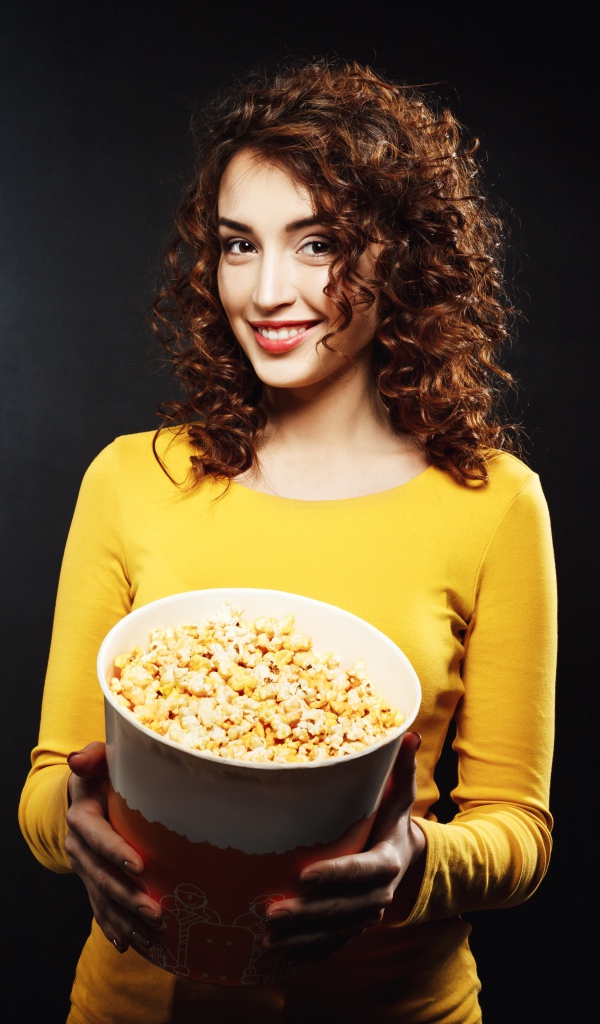 Улыбающаяся девушка с попкорном в руках на черном фоне 