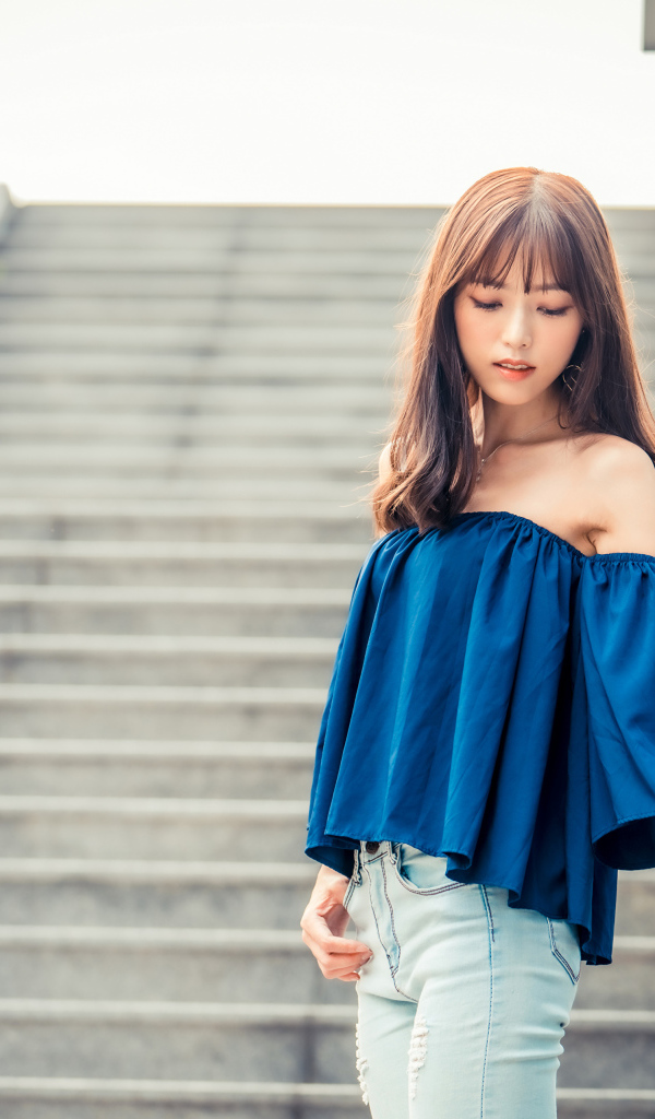 Стильная девушка азиатка с опущенной головой стоит на ступеньках 