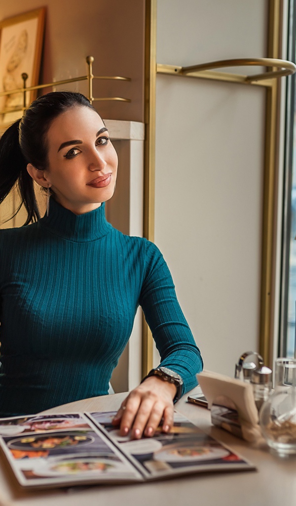 Стильная девушка в платье сидит в кафе у окна