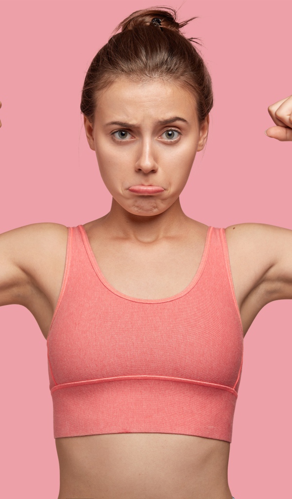 Расстроенная девушка без накаченных рук на розовом фоне