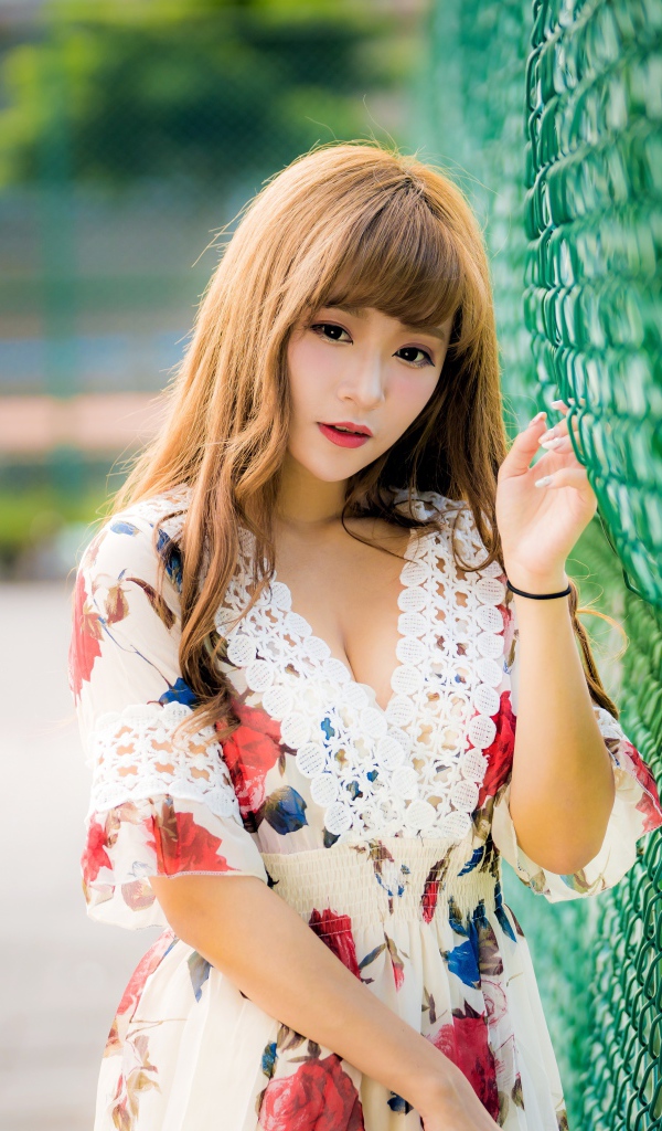 Молодая азиатка в платье у зеленой сетке 