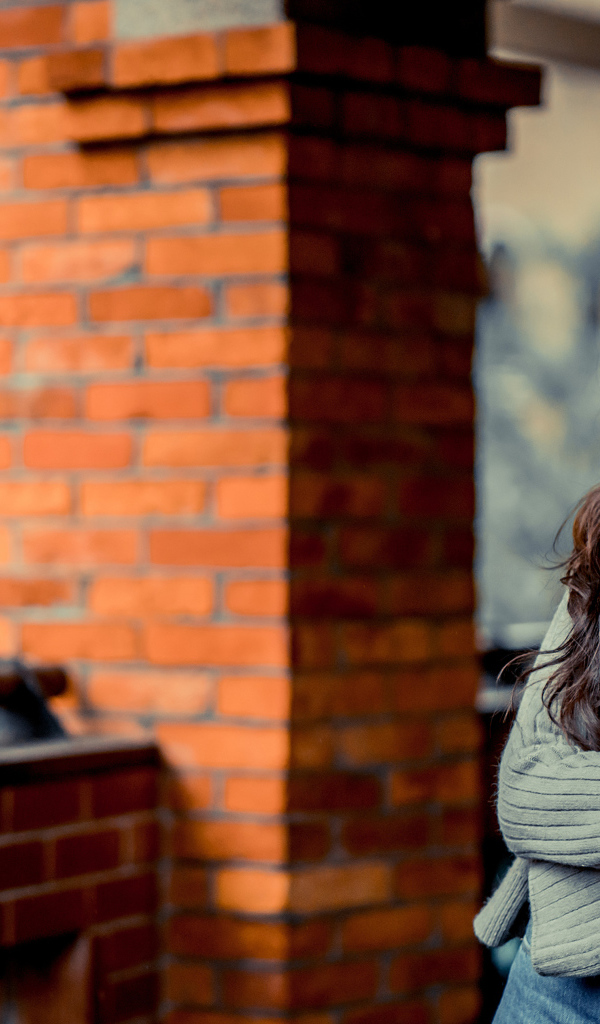 Молодая девушка азиатка в серой кофте у кирпичной стены 