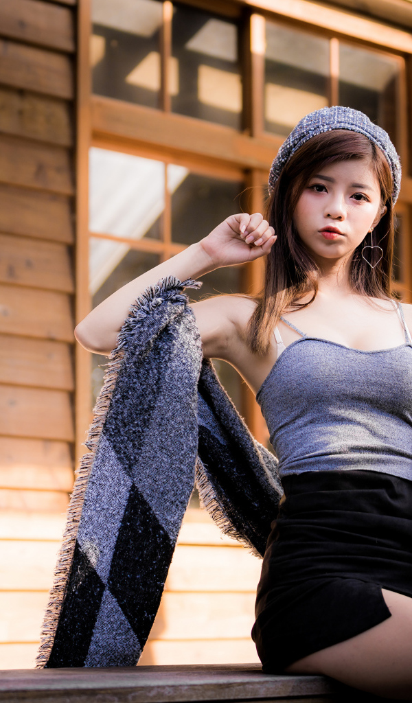 Молодая девушка азиатка в короткой юбке сидит на подоконнике 