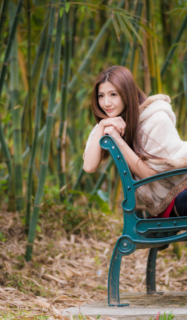Молодая девушка азиатка сидит на зеленой лавке 