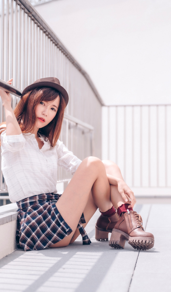 Молодая азиатка в короткой юбке сидит у перил 