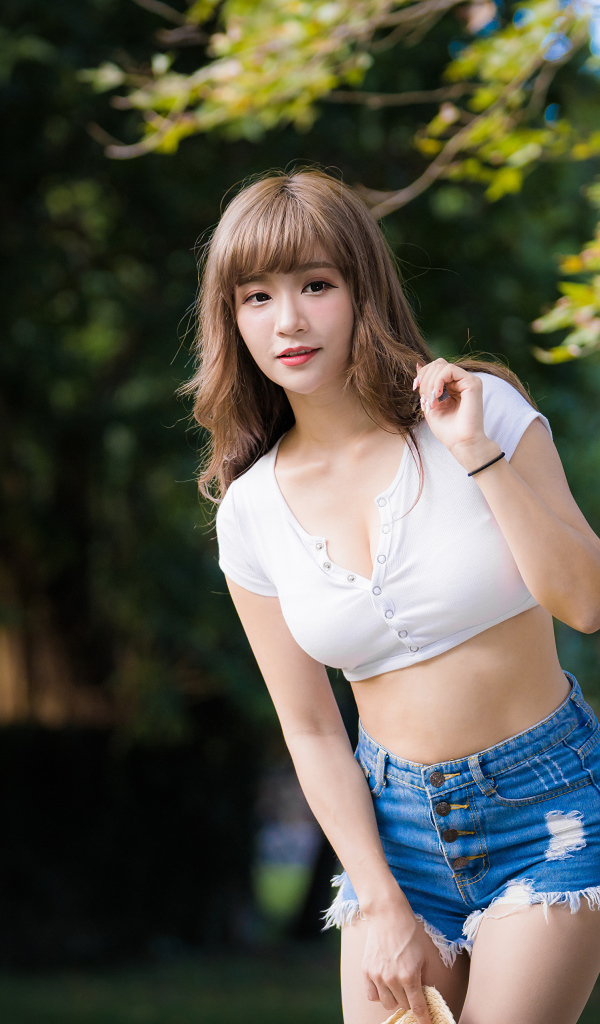 Молодая азиатка в белом топе и синих шортах  в парке