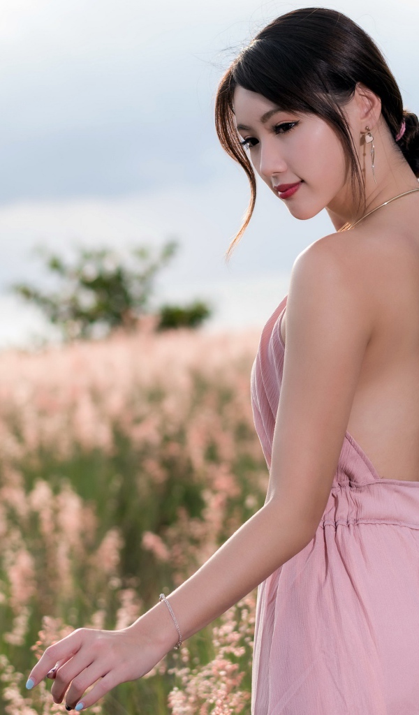 Молодая азиатка в розовом платье гуляет по полю с колосьями