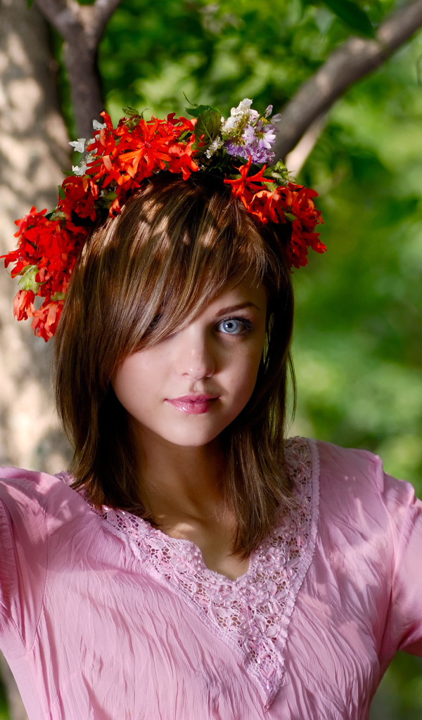 Молодая милая голубоглазая девушка с венком на голове у дерева