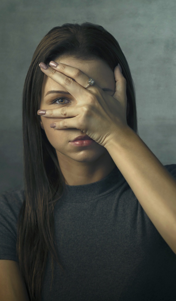 Молодая девушка закрыла лицо рукой на сером фоне