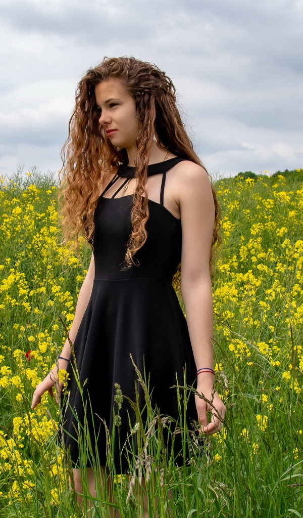 Молодая девушка в черном платье на поле с желтыми цветами