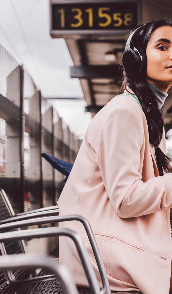 Молодая девушка в наушниках сидит на остановке