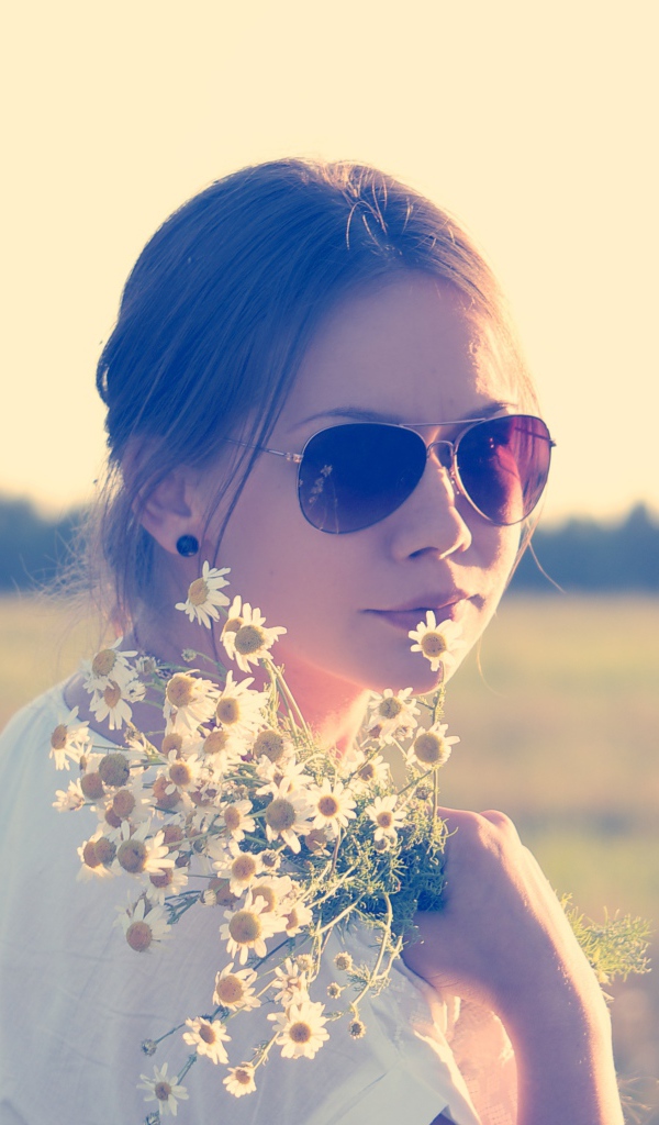 Молодая девушка в солнечных очках с букетом ромашек на поле