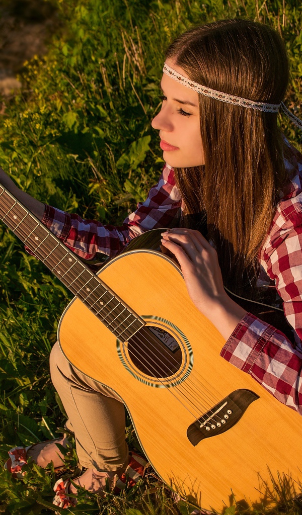Молодая девушка хиппи сидит с гитарой на траве 
