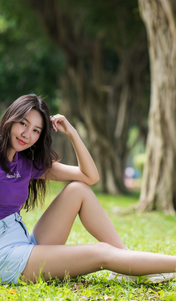 Молодая стройная азиатка сидит на земле в парке