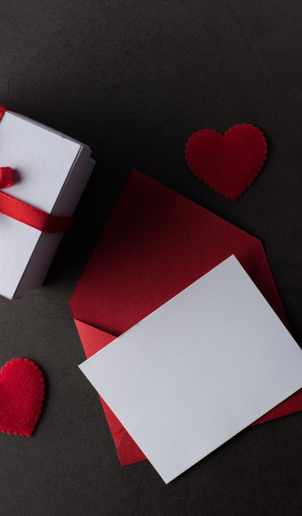 Конверт и подарок на сером столе с красными сердечками