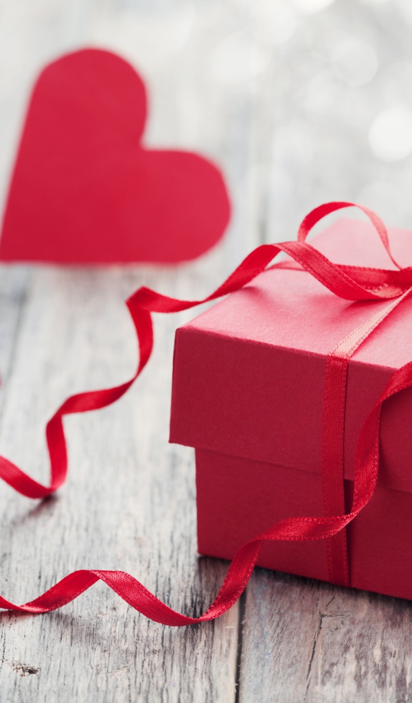 Красная коробка с подарком на столе с красными сердечками