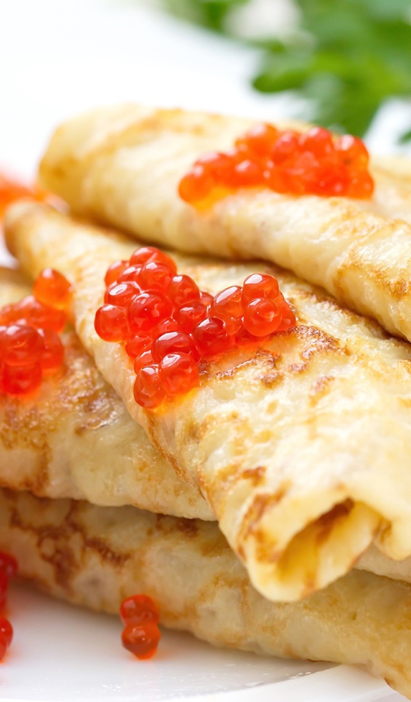 Аппетитные тонкие блины с красной икрой на тарелке с петрушкой угощение на Масленицу